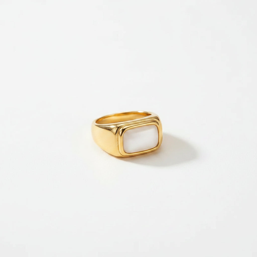 Gold ring with a white stone on a beige fabric background with flowers and stones.